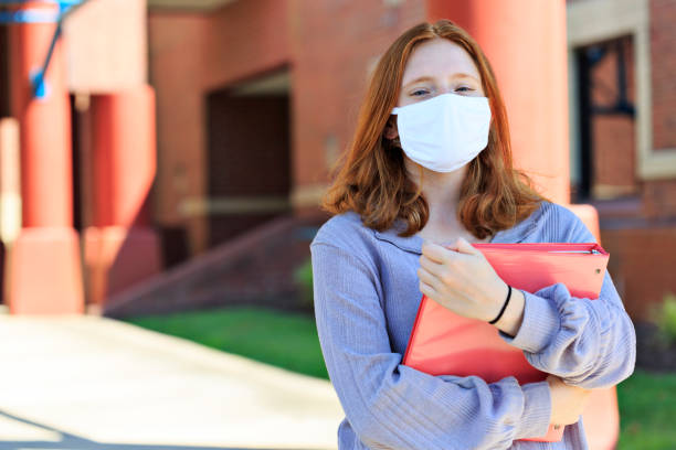 Front view of red-headed teen wearing mask on campus - fotografia de stock