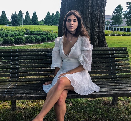 A young beautiful woman in a white dress sits on a park bench on a spring afternoon.