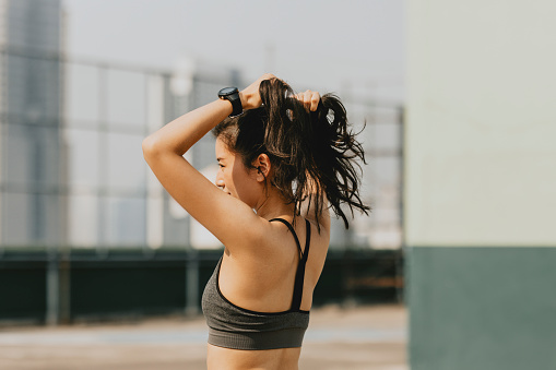 Outdoor shot of a young Asian woman tying her hair while working out outdoors.