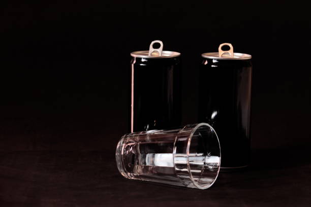 tasse en verre se trouvant devant deux boîtes en aluminium peintes en noir, sur un fond foncé. - tin glazed flash photos et images de collection
