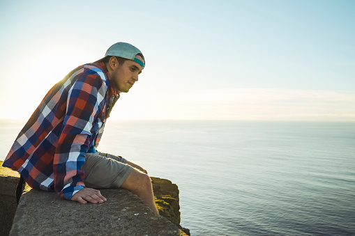 Young man sitting on the rocks of a mountain looking at the ocean