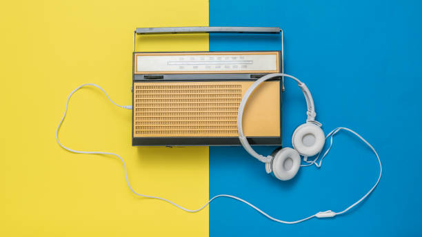 auriculares blancos conectados a una radio antigua sobre un fondo amarillo y azul. técnica vintage. - radio old fashioned antique yellow fotografías e imágenes de stock