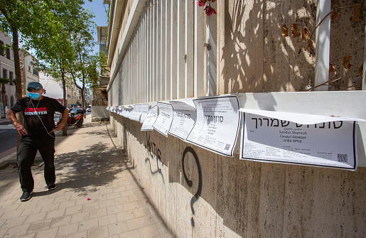 Tel Aviv, Israel - June 22, 2020: Obituaries were hung around the city to protest the murder of women. Elderly man wearing face mask walks around.