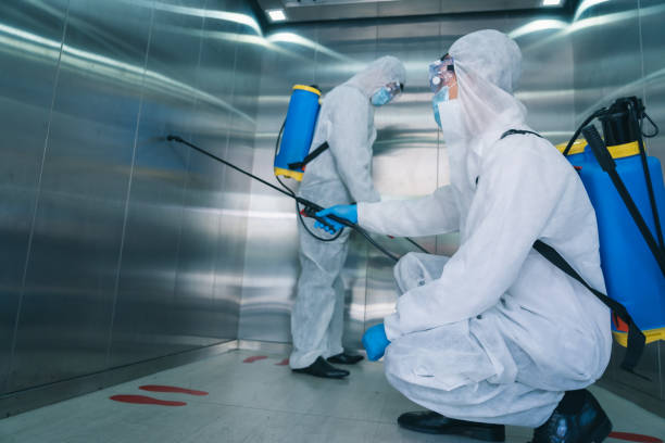 Man in virus protective suite and mask spraying alcohol cleaning covid19 infected elevator area stock photo