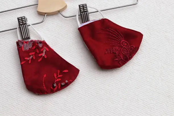 Photo of Ruby Red color of lace reusable face masks hanging on clothes hanger placed on brown background.