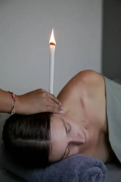 Woman receiving ear candle treatment at spa. Ear coning or thermal-auricular therapy.