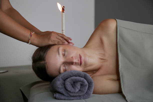 Woman receiving ear candle treatment at spa. Ear coning or thermal-auricular therapy. stock photo