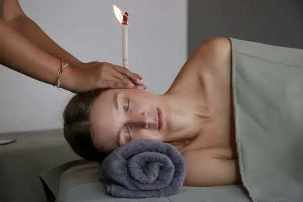 Woman receiving ear candle treatment at spa. Ear coning or thermal-auricular therapy.