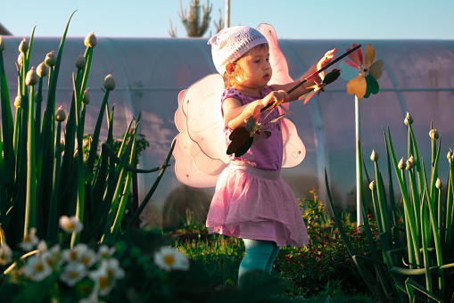 Cute baby girl playing in the garden with a wind spinner on the background of the sunset.