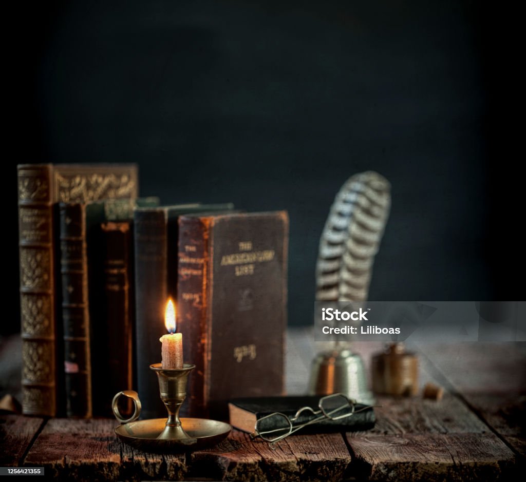 Vintage Books on an Old Wood Table Vintage study area with books, quill pen and candle on an old wood desk against a black background. Book Stock Photo
