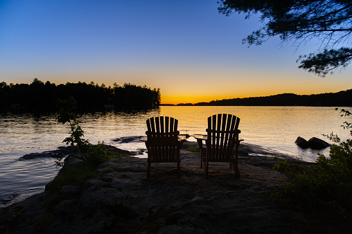 Adirondack chairs facing the waters of a lake at sunset in Muskoka, Ontario Canada.