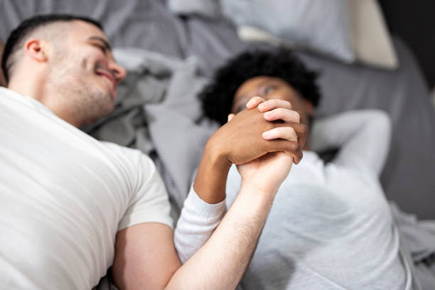 istock Young multiethnic couple holding hands while lying in bed in morning 1256433612