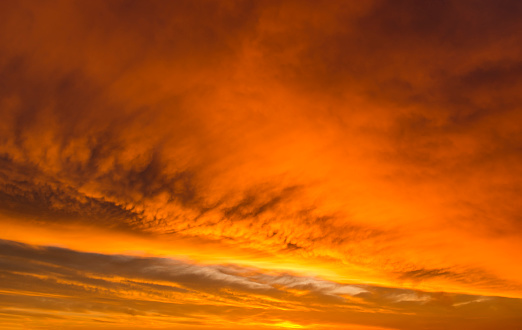 Dramatic sky with radiating and glowing altocumulus clouds in red, orange, yellow and golden colours. A full frame image of the sky only.