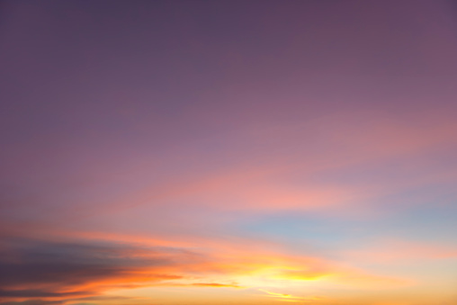 The morning glows yellow, orange and  golden at the lower part of the image. And behind a small patch of blue sky, the cloudscape colours radiate red and smoothly merge into the dark sky at the top of the image. A sky only and full-frame image.