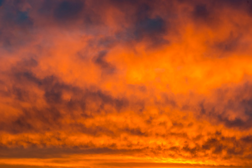 Dramatic sky with radiating and glowing altocumulus clouds in red, orange, yellow and golden colours. A full frame image of the sky only.