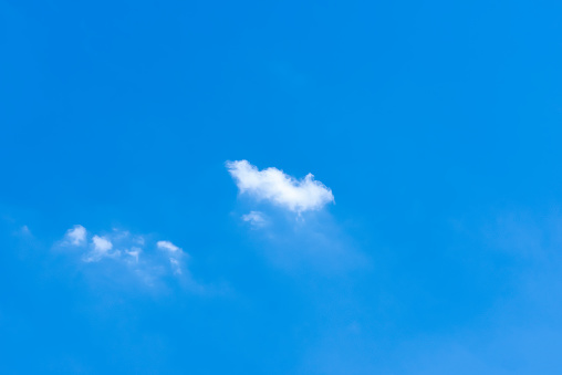 It is a clear sunny summer day. Only two little pure white cumulus clouds float in the clear blue skyscape. They are about to dissolve. A full-frame sky only image with copy space.