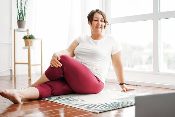 adult charming brunette woman plus size body positive practice yoga with laptop at the home - body positive imagens e fotografias de stock