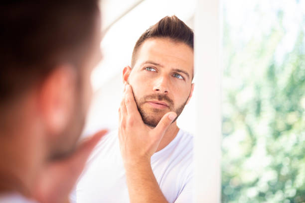 istock Handsome young man standing in front of bathroom mirror and looking his face 1256456310