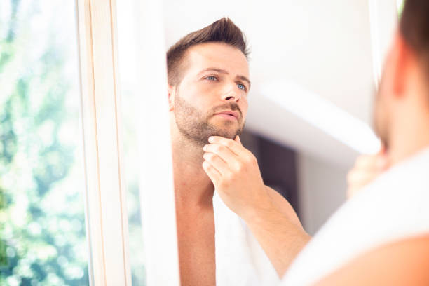 istock Handsome young man standing in front of bathroom mirror and looking his face 1256456311