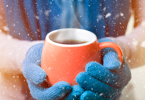 The woman's hands in mittens hold a cup of hot drink, tea or coffee to keep warm from the cold.