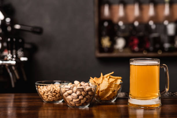Snacks for client. Pistachios, nuts and chips in glass plates and mug of light beer in interior of pub, free space