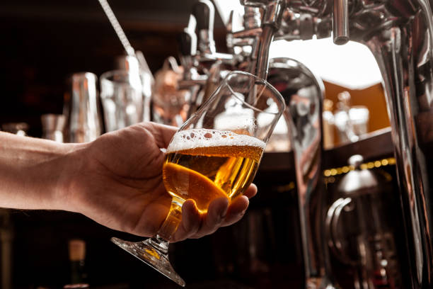 istock Client service at bar. Bartender pours a beer from tap in glass in interior 1256458845