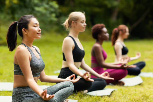 Concentrated multinational ladies meditating or doing breathing exercises on yoga practice outside, empty space Concentrated multinational ladies meditating or doing breathing exercises on yoga practice outside, free space mudra stock pictures, royalty-free photos & images