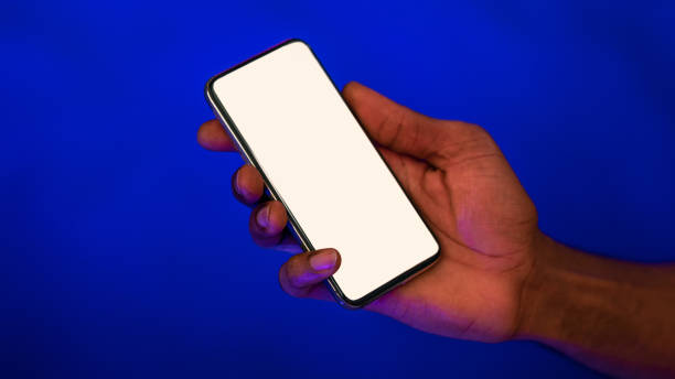 istock Male Hand Holding Cellphone With Empty Screen, Blue Background, Panorama 1256460794
