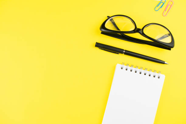 istock Black glasses, pen, notepad and colorful clips on yellow background. Flat lay. Copy space. Workplace in the office. 1256462136