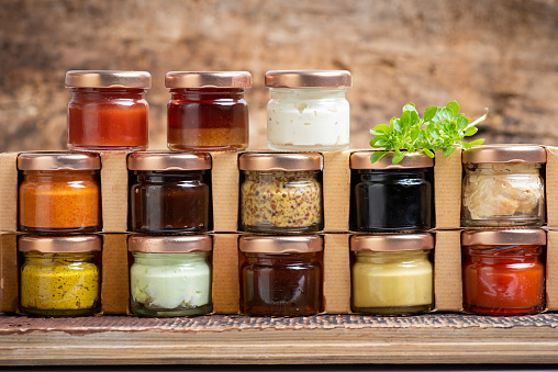 Large collection of sauces and spiced spreads in small jars on a shelf. Food ingredients and dressings as mayo ketchup mustard soy sauce and many more