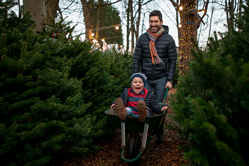 A Father giving his son a wheelbarrow ride at a Christmas market in Northeastern England. They are wearing warm clothing and having fun.