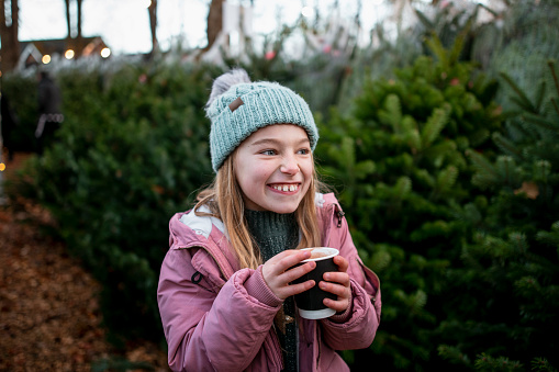 A young girl wearing warm clothing at a Christmas market in Northeastern England. She is enjoying a festive hot chocolate to keep warm.