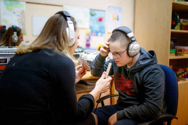 Teen boy with special needs working with speech therapist Special needs teenger boy working with speech therapist in audio laboratory, he is wearing headphones while speech therapist is hoding microphone in front of him while showing him pictures on flash cards special education stock pictures, royalty-free photos & images