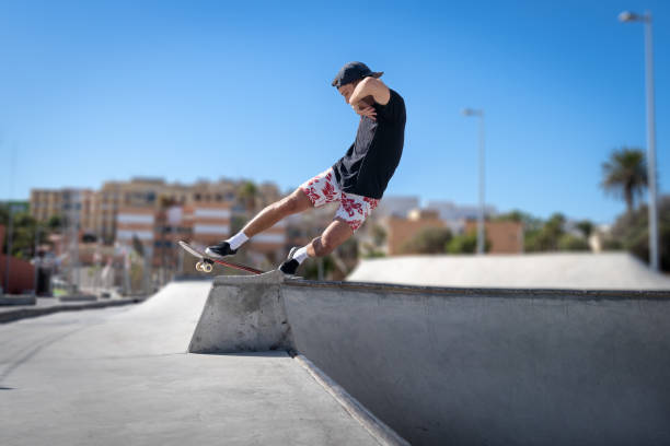 il giovane skateboarder fa un trucco chiamato "rock to fakie" ai margini di una piscina in uno skate park. vista laterale - fakie foto e immagini stock