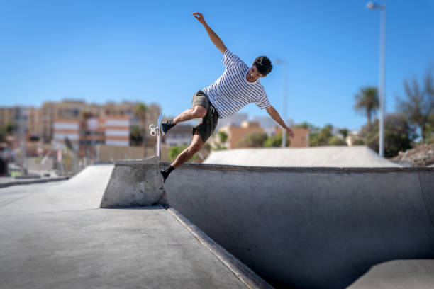 il giovane skateboarder fa un trucco chiamato "rock to fakie" ai margini di una piscina in uno skate park - fakie foto e immagini stock