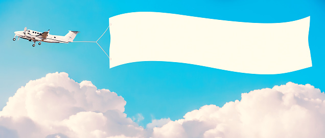 Airplane with white banner for advertising among the clouds. Tinted vintage style. Mockup for your text