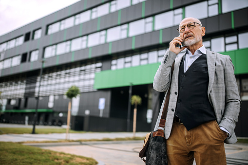 Senior businessman in front of his company, talking on a phone