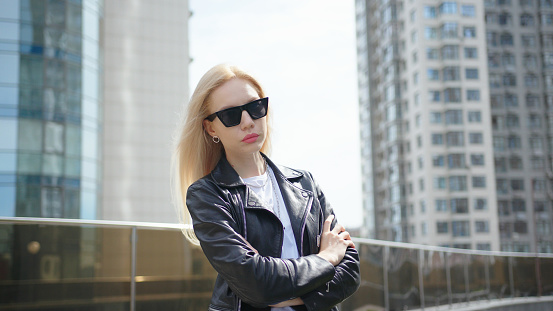 Portrait of beautiful stylish mixed race woman looking confident. Wearing black clothes and sunglasses. Scyscrappers architecture urban city background.