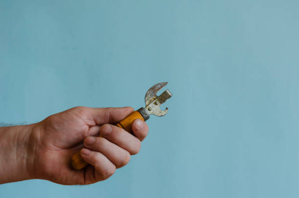 Man's hands hold an old can opener with a wooden handle.
