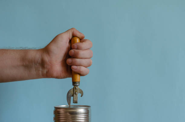 istock Man's hands open a tin can with an old can opener with a wooden handle. 1256480866