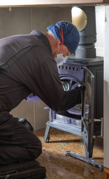 istock Chimney sweep cleaning a log mixed fuel burner with face covering and protective clothes. 1256485278
