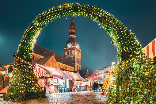 Riga, Latvia. Traditional Christmas Market On Dome Square With Cathedral. Famous Landmark In Winter Evening Night In Festive Illuminations Lighting