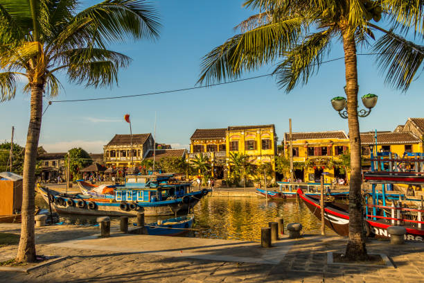 A view across the river from the south bank in Hoi An Vietnam, A view across the river from the south bank in Hoi An Vietnam, with palm trees and boats in the foreground thu bon river stock pictures, royalty-free photos & images