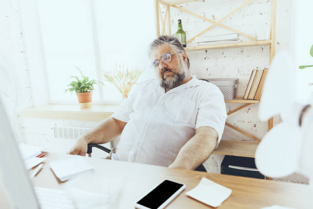 istock Businessman, manager in office with computer and fan cooling off, feeling hot, flushed 1256489690