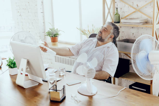 istock Businessman, manager in office with computer and fan cooling off, feeling hot, flushed 1256489703