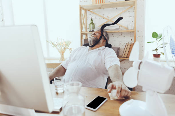 istock Businessman, manager in office with computer and fan cooling off, feeling hot, flushed 1256489705