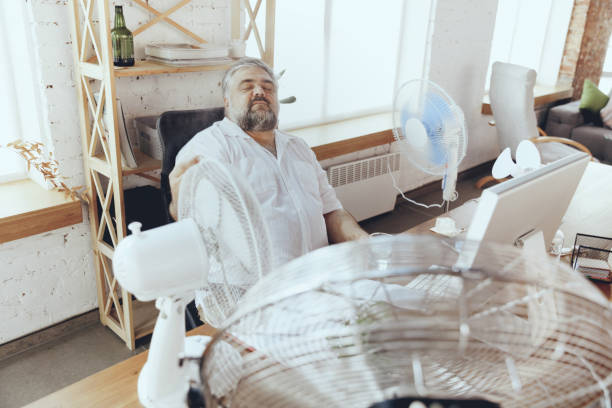istock Businessman, manager in office with computer and fan cooling off, feeling hot, flushed 1256489716