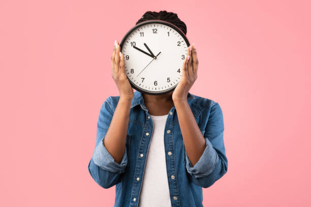 african girl holding clock in front of face, pink background - clock face clock deadline human hand imagens e fotografias de stock