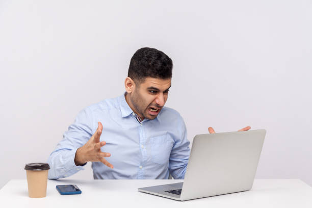 istock Irritated businessman sitting office workplace, looking at laptop with furious expression, shouting angry 1256493513