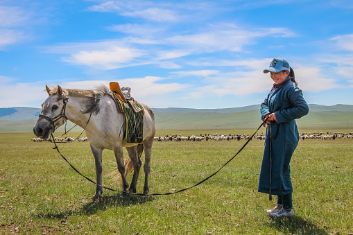 A happy female Mongolian herder and her horse, with her cattle in the background - Moron, Mongolia - July 14th 2014: